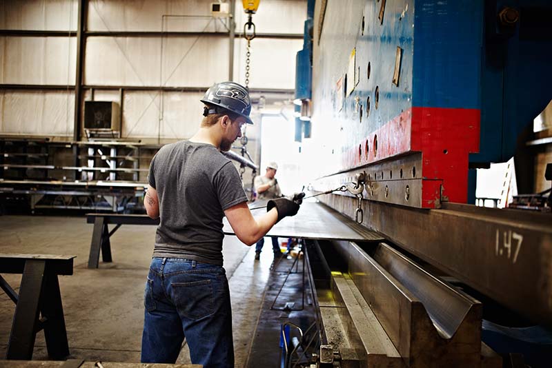 A metal workers using an industrial press brake of a large steel plate